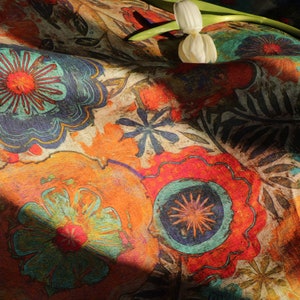 May include: A colorful fabric with a floral pattern. The fabric features a variety of flowers in shades of orange, red, blue, and green. The fabric is textured and has a vintage look.