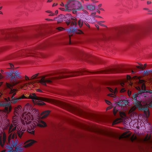 Peut inclure: Tissu rouge à motif floral. Les fleurs sont dans des tons de rose, violet, bleu et jaune. Le tissu a un léger brillant.