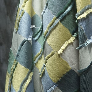 Puede incluir: Primer plano de una tela con un patrón de rombos en tonos azules, verdes y amarillos. La tela tiene un borde deshilachado, lo que le da un aspecto texturizado.