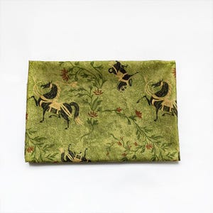 Może przedstawiać: Złożona zielona tkanina z powtarzającym się wzorem czarnych i złotych koni, kwiatowych winorośli i czerwonych kwiat&oacute;w. Tkanina ma lekko teksturowany wygląd na białym tle.