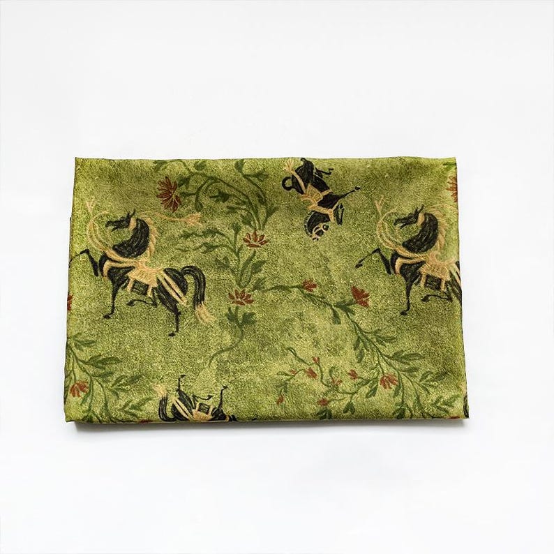 Może przedstawiać: Złożona zielona tkanina z powtarzającym się wzorem czarnych i złotych koni, kwiatowych winorośli i czerwonych kwiat&oacute;w. Tkanina ma lekko teksturowany wygląd na białym tle.