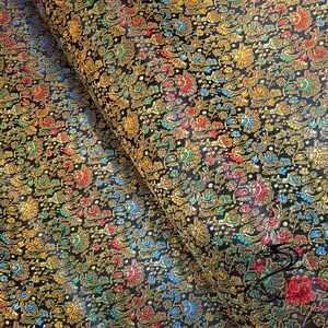 以下が含まれることがあります： 金色、赤色、青色、緑色の花柄が施された黒い布。布は、質感のある浮き出たデザインで織られています。