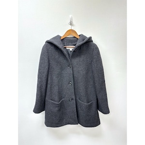May include: A dark grey hooded coat with a button-up front and two front pockets. The coat is suspended on a wooden hanger against a white wall. The coat's fabric appears to be a soft wool blend.