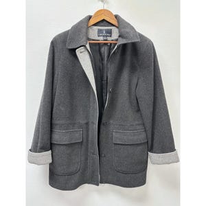May include: A charcoal gray wool coat with a notched collar, two front pockets, and a zip-up closure. The coat has gray cuffs and a gray lining. The London Fog logo is visible on the back of the collar.
