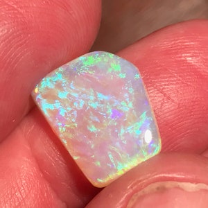 May include: A light blue and green opal gemstone with a rough, irregular shape. The opal is iridescent and has a white base.