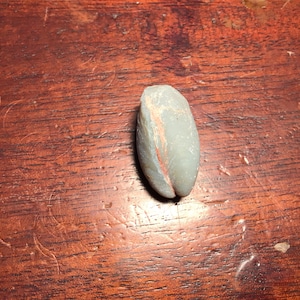 Puede incluir: Una piedra lisa, ovalada y gris con una franja roja que recorre el centro.