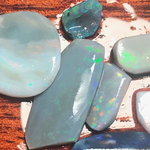 May include: A collection of six opal gemstones in various shapes and sizes. The opals are a light blue-grey colour with iridescent flashes of green, blue, and red.