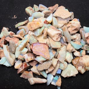 May include: A collection of raw opal gemstones in various shapes and sizes. The opals display a range of colours, including white, blue, orange, and brown. The gemstones are scattered on a black surface.