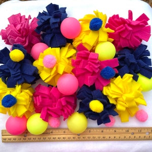 May include: A collection of colourful felt toys for dogs. The toys are in the shape of flowers and have different colours, including pink, yellow, blue, and navy. There are also several small, brightly coloured balls.