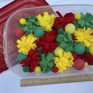 May include: A clear plastic container filled with red, yellow, and green felt balls and pom-poms. The container has a red lid.
