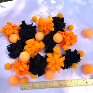 May include: A collection of orange and black felt pom-poms and orange balls. The pom-poms are in various shapes and sizes. The balls are approximately 2.5 cm in diameter.