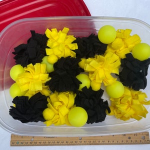 May include: A clear plastic container filled with yellow and black felt balls and yellow pom-poms.