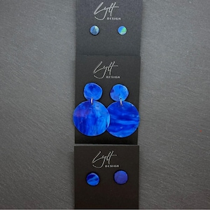 May include: Three sets of blue earrings on black display cards labelled Lytt Design. The top and bottom sets are small circular studs. The middle set features two circular blue discs of varying sizes connected by a silver-toned metal jump ring.