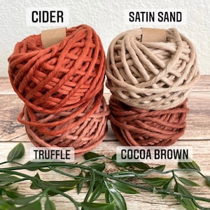May include: Four spools of macrame cord in various colors: Cider, Satin Sand, Truffle, and Cocoa Brown. The Cider spool is a reddish-orange, while Satin Sand is a light beige. Truffle is a medium brown, and Cocoa Brown is a dark brown. The spools are stacked.