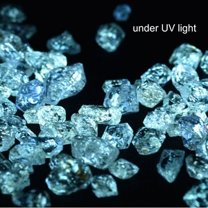 May include: A close-up of many small, clear, faceted crystals under a UV light. The crystals are glowing a bright blue color.