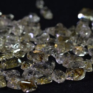 May include: A close-up of a group of clear quartz crystals with golden inclusions. The crystals are faceted and have a variety of shapes and sizes.