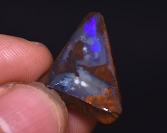May include: A triangular piece of opal with a brown backing. The opal has a blue and white iridescent sheen.