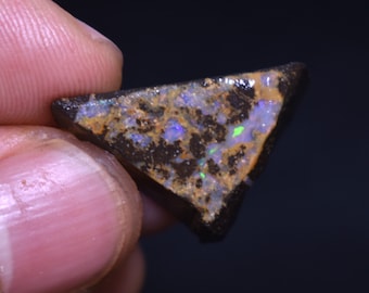 May include: A triangular piece of rough opal with a dark brown matrix. The opal has a variety of colors including green, blue, and purple.