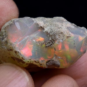 May include: A rough, natural opal with a milky white body and flashes of iridescent red, orange, and green.