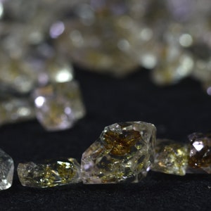 May include: Close-up of a group of clear quartz crystals with brown inclusions. The crystals are faceted and have a natural, rough texture.