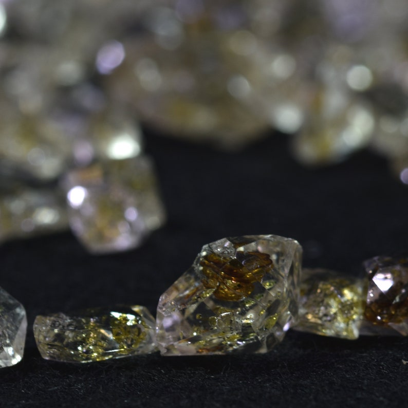 May include: Close-up of a group of clear quartz crystals with brown inclusions. The crystals are faceted and have a natural, rough texture.