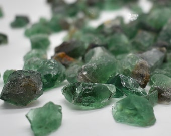 May include: A collection of green and gray gemstone chips. The chips are irregularly shaped and have a translucent appearance.