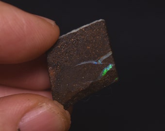 May include: A small, rough, brown rock with iridescent green and blue opal inclusions.