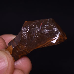 May include: A brown and black opal with a red and white flash of color. The opal is rough and has a natural shape.