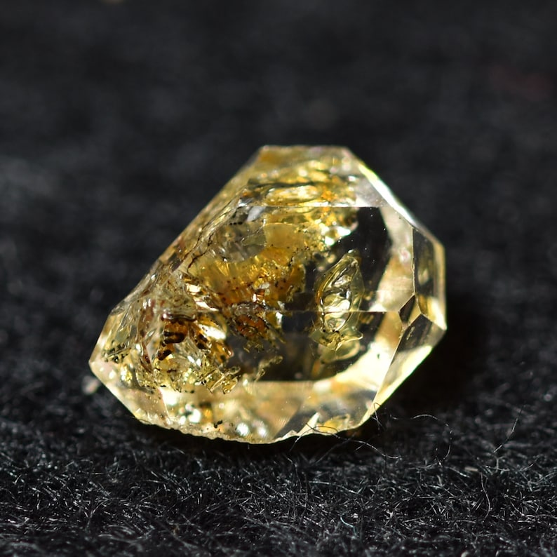 May include: A clear quartz crystal with inclusions of golden brown minerals. The crystal is faceted and has a pointed shape.