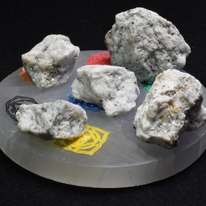 Könnte beinhalten: Fünf raue, weiße und graue Steine mit goldenen Flecken auf einer weißen, runden, dekorativen Oberfläche mit bunten Designs.