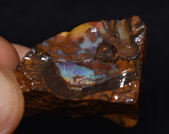 May include: A rough, brown, and black rock with a patch of iridescent opal showing blue, green, and yellow colors.