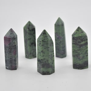 May include: Five polished gemstone towers. The stones are mainly green with black and red inclusions. Each tower has a pointed top and a rectangular base. The gemstones are arranged against a white backdrop.