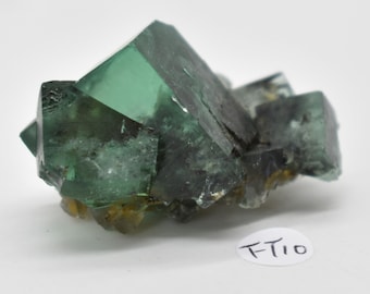 May include: A cluster of green fluorite crystals with a dark green hue and some clear areas. The crystals are clustered together in a rough, natural formation.