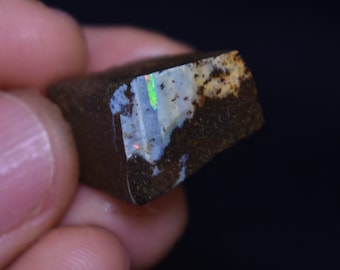 May include: A rough, dark brown rock with a small patch of iridescent opal. The opal shows flashes of green, blue, and white.