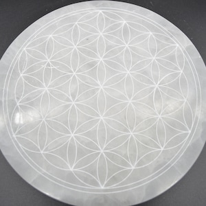 Peut inclure: Une plaque de recharge en sélénite blanche avec un motif de fleur de vie gravé à la surface.