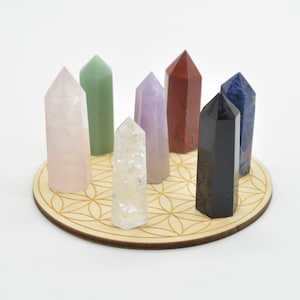 Könnte beinhalten: Ein Satz von acht Kristallspitzen, die in einem Kreis auf einem Holz-Lebensblume-Mandala angeordnet sind. Die Spitzen sind aus klarem Quarz, Rosenquarz, Amethyst, grünem Aventurin, rotem Jaspis, schwarzem Obsidian, blauem Sodalith und Lapislazuli.