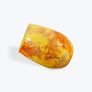 May include: A yellow stemless wine glass with a textured surface and gold and orange accents. The glass has a unique shape and is tilted slightly to the side. The text "@Shi.Wines" is visible on the side of the glass.
