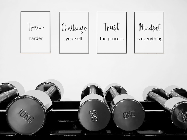 May include: Black and white motivational posters with the text "Train harder", "Challenge yourself", "Trust the process", and "Mindset is everything" hanging on a white wall above a rack of silver dumbbells. The dumbbells are labeled with weights in kilograms.