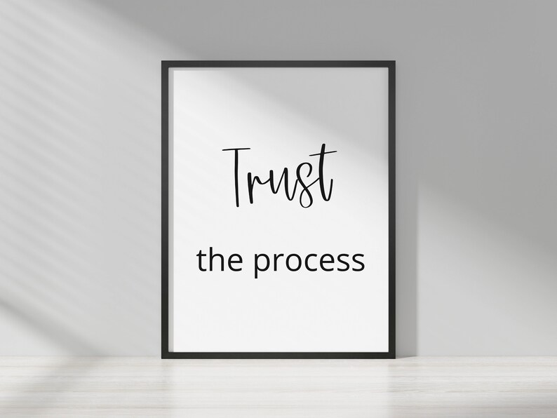 May include: A black framed print with white background and black text that reads "Trust the process".