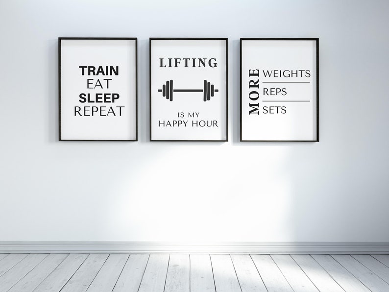 May include: Three framed prints with black frames and white backgrounds. The prints feature black text related to fitness: "TRAIN EAT SLEEP REPEAT", "LIFTING IS MY HAPPY HOUR" with a barbell graphic, and "MORE WEIGHTS REPS SETS".
