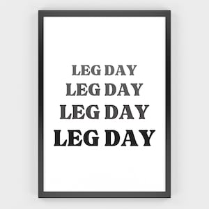 May include: A framed print with the words "LEG DAY" in a bold, sans-serif font. The text is stacked four times, with the color of the text transitioning from light gray to black. The frame is black, and the background is white.
