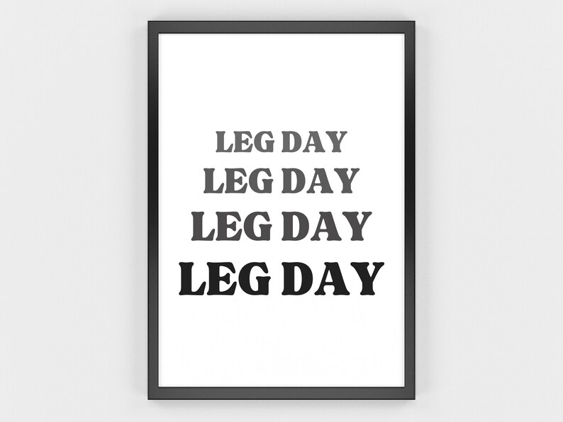 May include: A framed print with the words "LEG DAY" in a bold, sans-serif font. The text is stacked four times, with the color of the text transitioning from light gray to black. The frame is black, and the background is white.