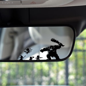 May include: Black vinyl car decal featuring a cartoon battle scene. A large, club-wielding monster is chasing smaller figures, including an archer, a wizard, and a warrior. The decal is designed to be applied to a car's rearview mirror.