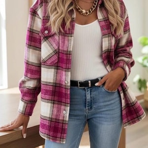 Könnte beinhalten: Ein rosa-weiß kariertes Flanellhemd mit zwei Brusttaschen. Das Hemd wird über einem weißen Tanktop getragen und mit einer blauen Jeans kombiniert. Ein schwarzer Gürtel und eine goldene Halskette vervollständigen den Look.