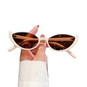 Op de afbeelding: Witte cat-eye zonnebril met bruine glazen. De zonnebril heeft een unieke halvemaanvorm en wordt in een hand gehouden.