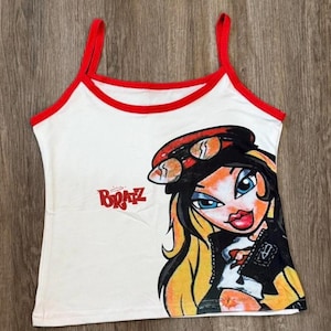 Op de afbeelding: Wit tanktop met rode bies en een afbeelding van een cartoonmeisje met blond haar dat een rode hoed en een zonnebril draagt. De afbeelding zegt "Bratz" in de linkerbovenhoek.