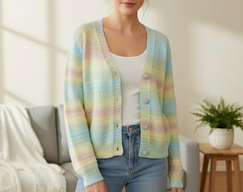 Op de afbeelding: Een pastelkleurig gestreept vest in tinten blauw, geel en roze. De trui heeft een V-hals, een knoopsluiting en decoratieve knopen. Het model draagt een witte tanktop en een blauwe jeans. Het vest is een lichtgewicht breisel.