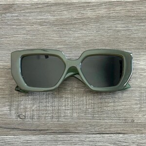Puede incluir: Un par de gafas de sol cuadradas de color verde oscuro con un marco grueso.