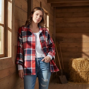 Puede incluir: Una camisa chaqueta de franela a cuadros rojos, blancos y azul marino con botones. La chaqueta se lleva sobre una camisa blanca de manga larga y se combina con vaqueros azules. El fondo es una estructura de madera con una ventana.