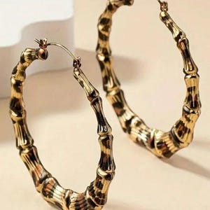 May include: Gold hoop earrings with a leopard print design. The earrings are made of a bamboo-like material.